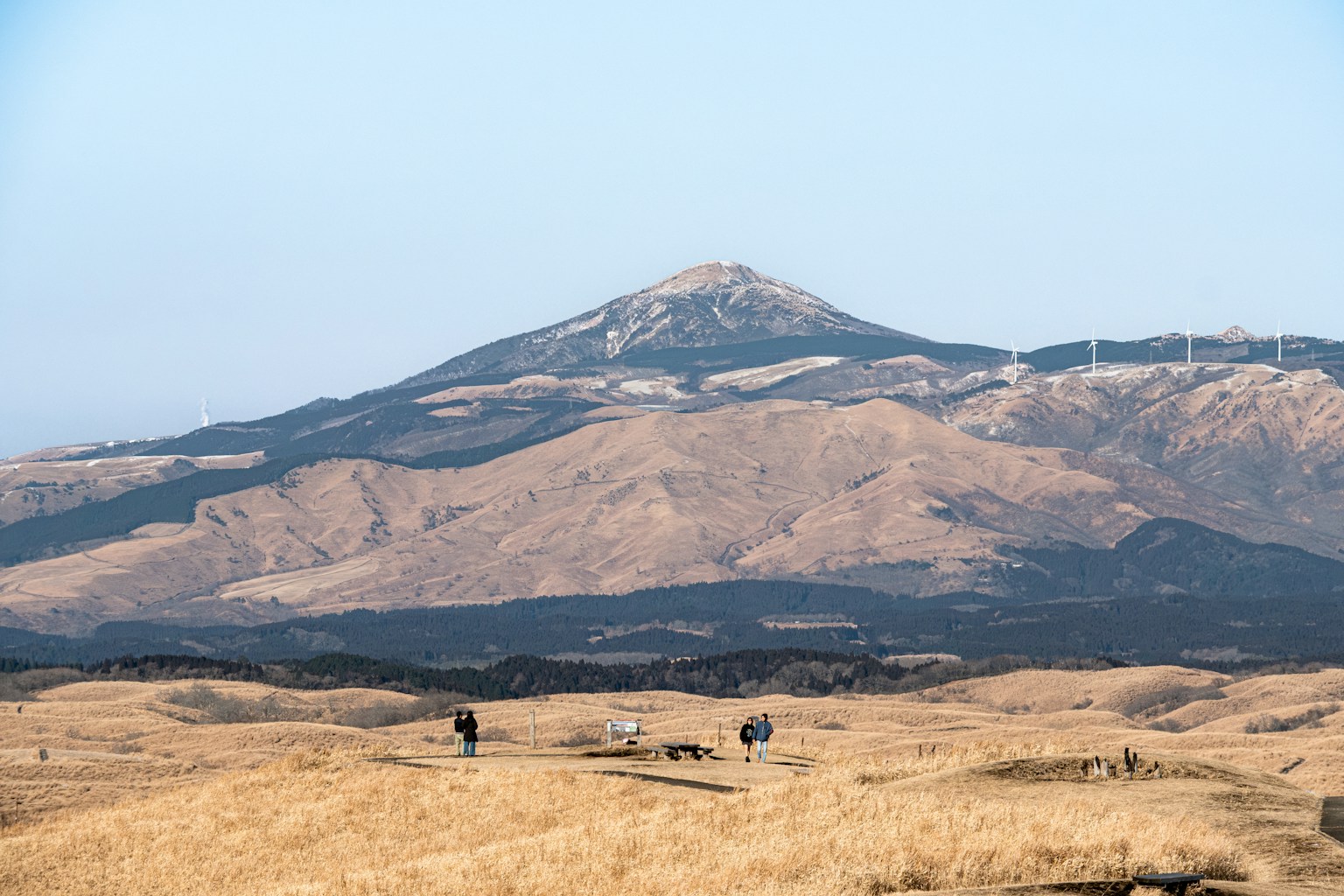 People walking in a dry grassy field with mountains behind. (Photo by Tuan P. on Unsplash)
