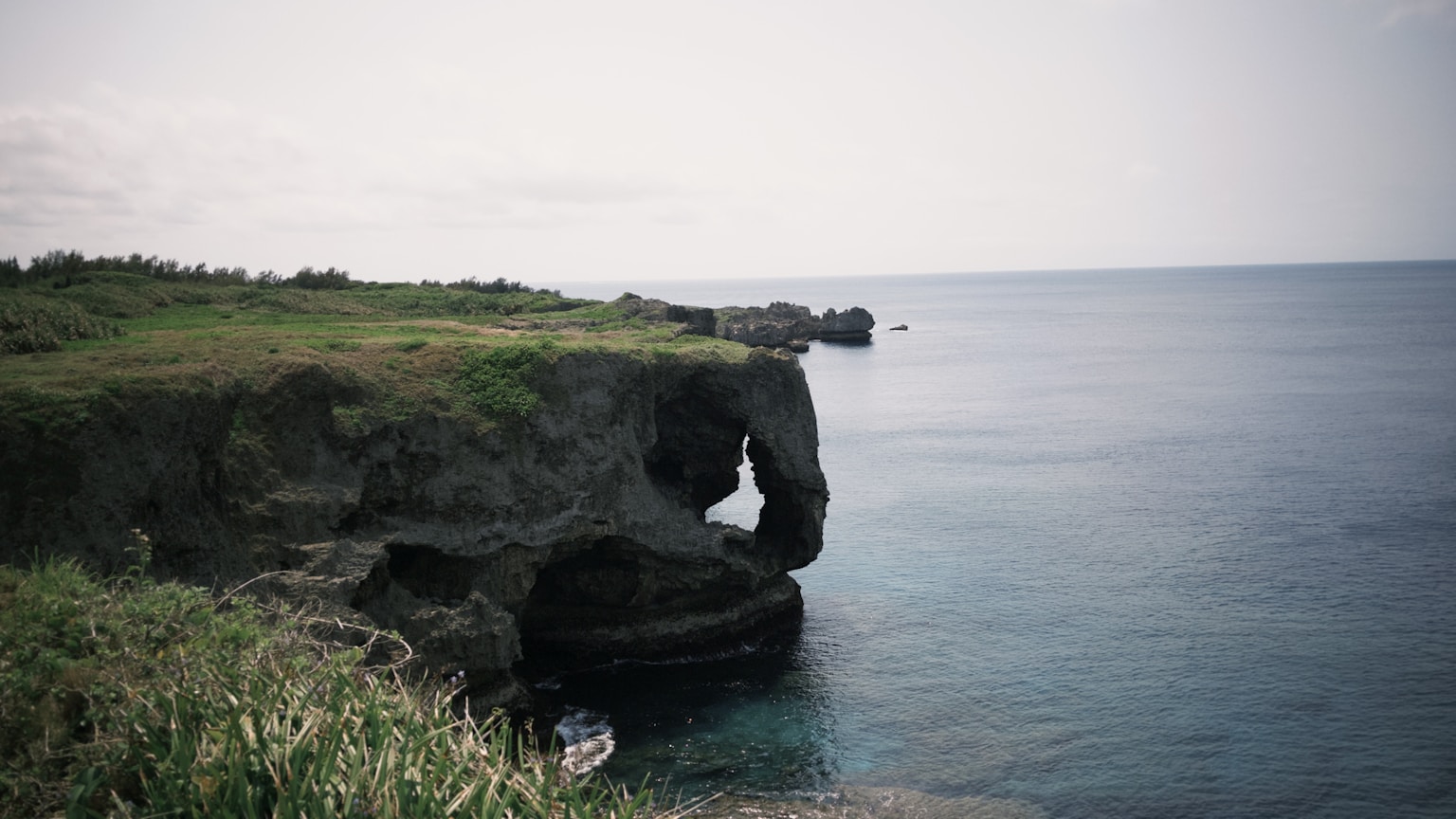 Jagged cliffs overlook a calm, blue ocean. (Photo by Monineath Horn on Unsplash)