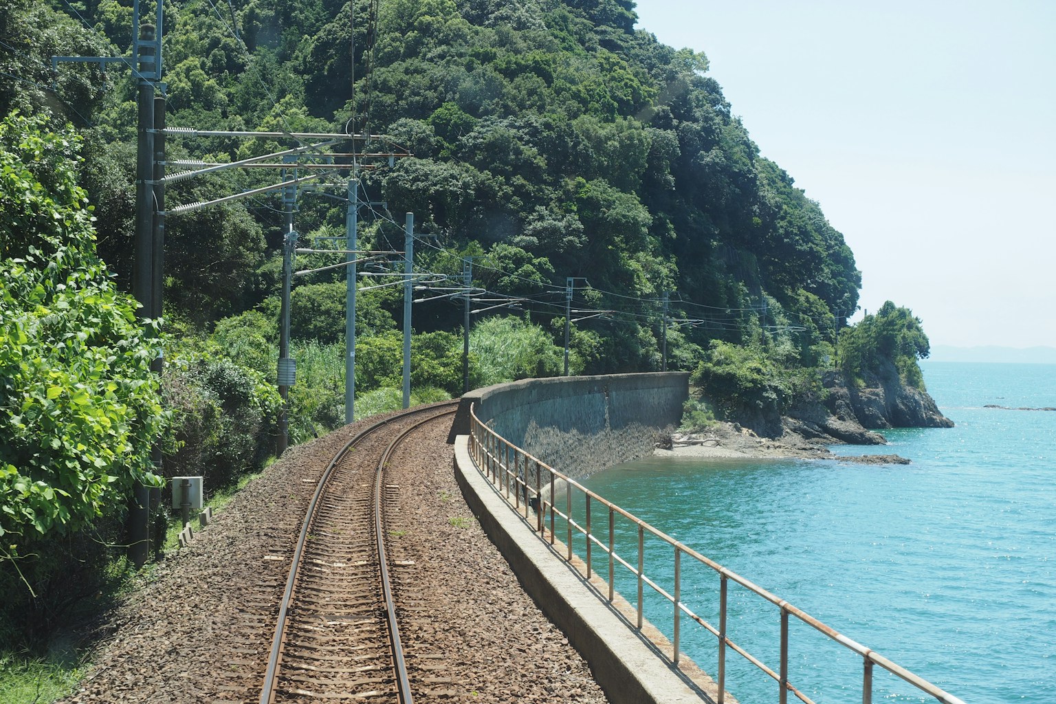 Train tracks curve along a rocky coastline beside the ocean. (Photo by Bobby Youstra on Unsplash)