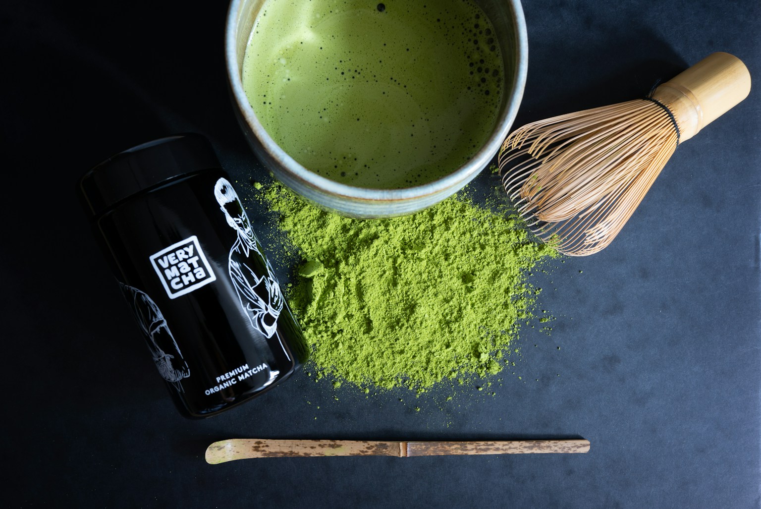 Matcha tea powder, whisk, and cup on dark surface (Photo by Very Matcha on Unsplash)