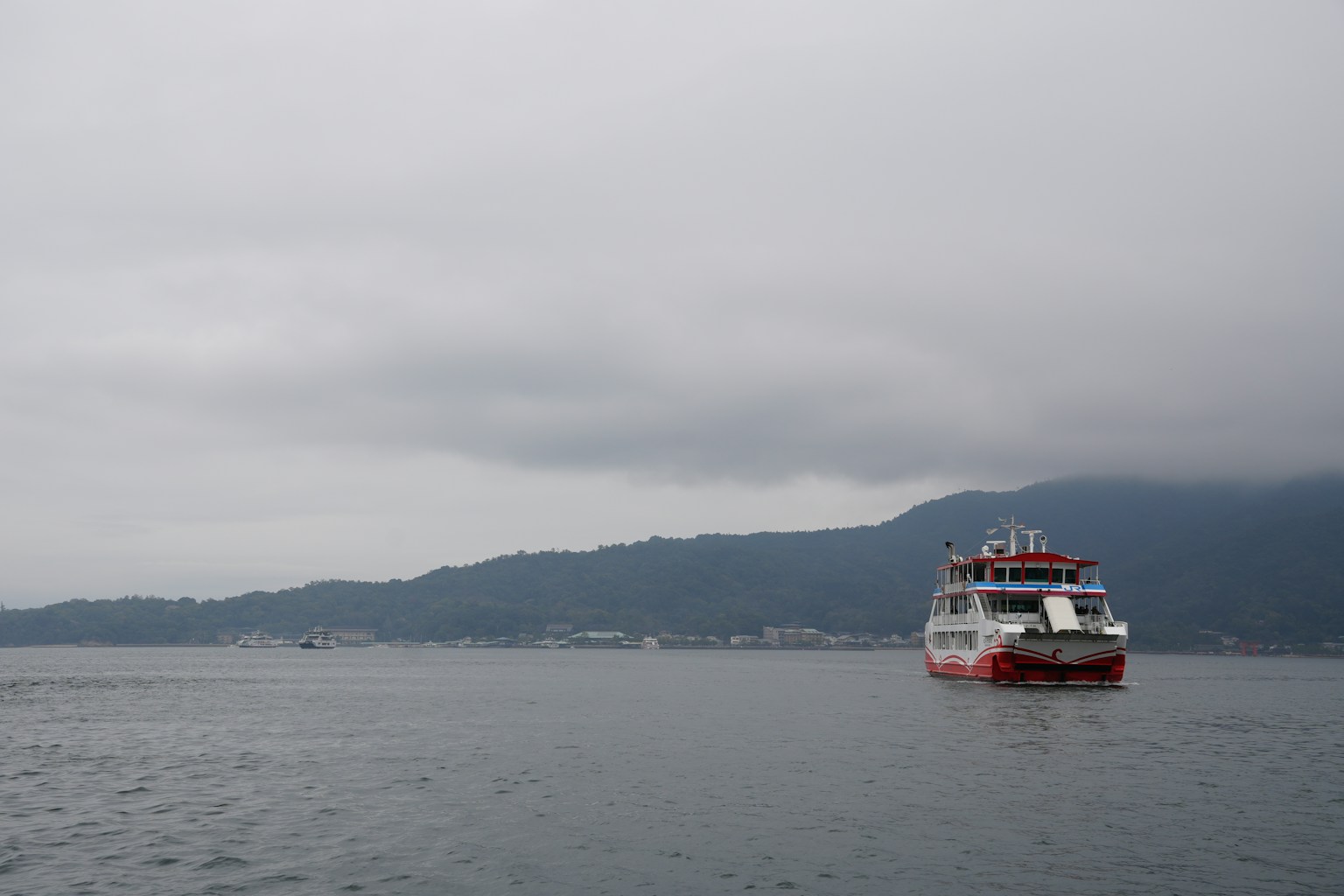 A ferry sails on calm water under a cloudy sky. (Photo by Dmitry Romanoff on Unsplash)