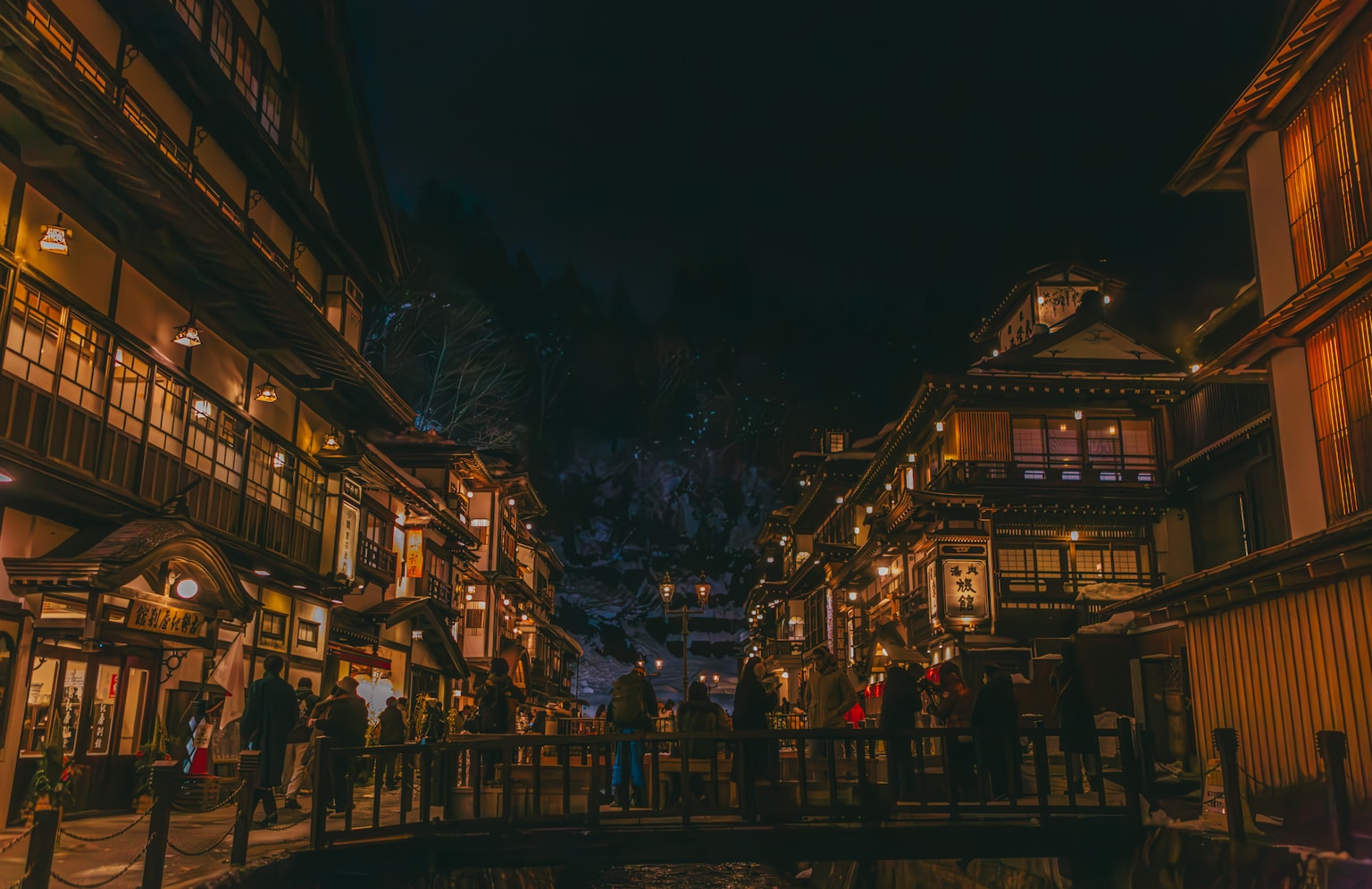A city street at night with people walking on the sidewalk (Photo by HANVIN CHEONG on Unsplash)