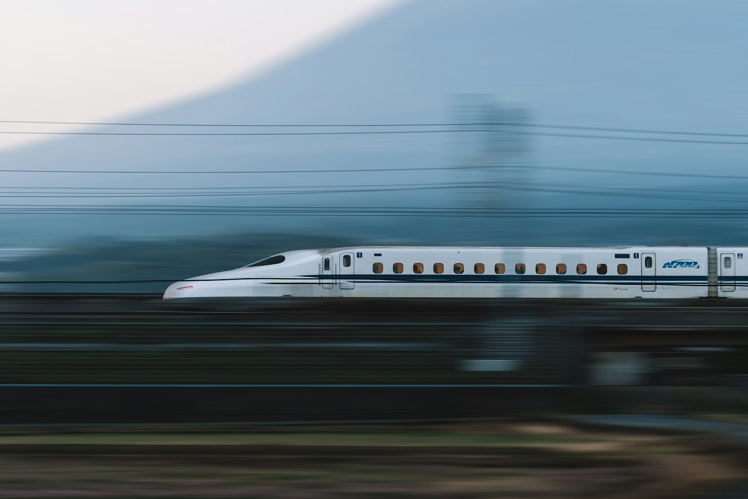 A white bullet train speeds past a mountain. (Photo by Spenser Sembrat on Unsplash)