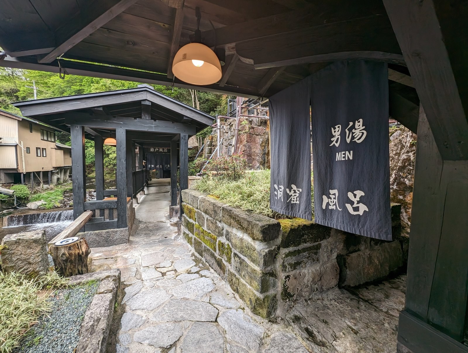 The entrance to a cave bath (dokutsu-buro) beside a stream at Kurokawa Onsen, with a noren curtain