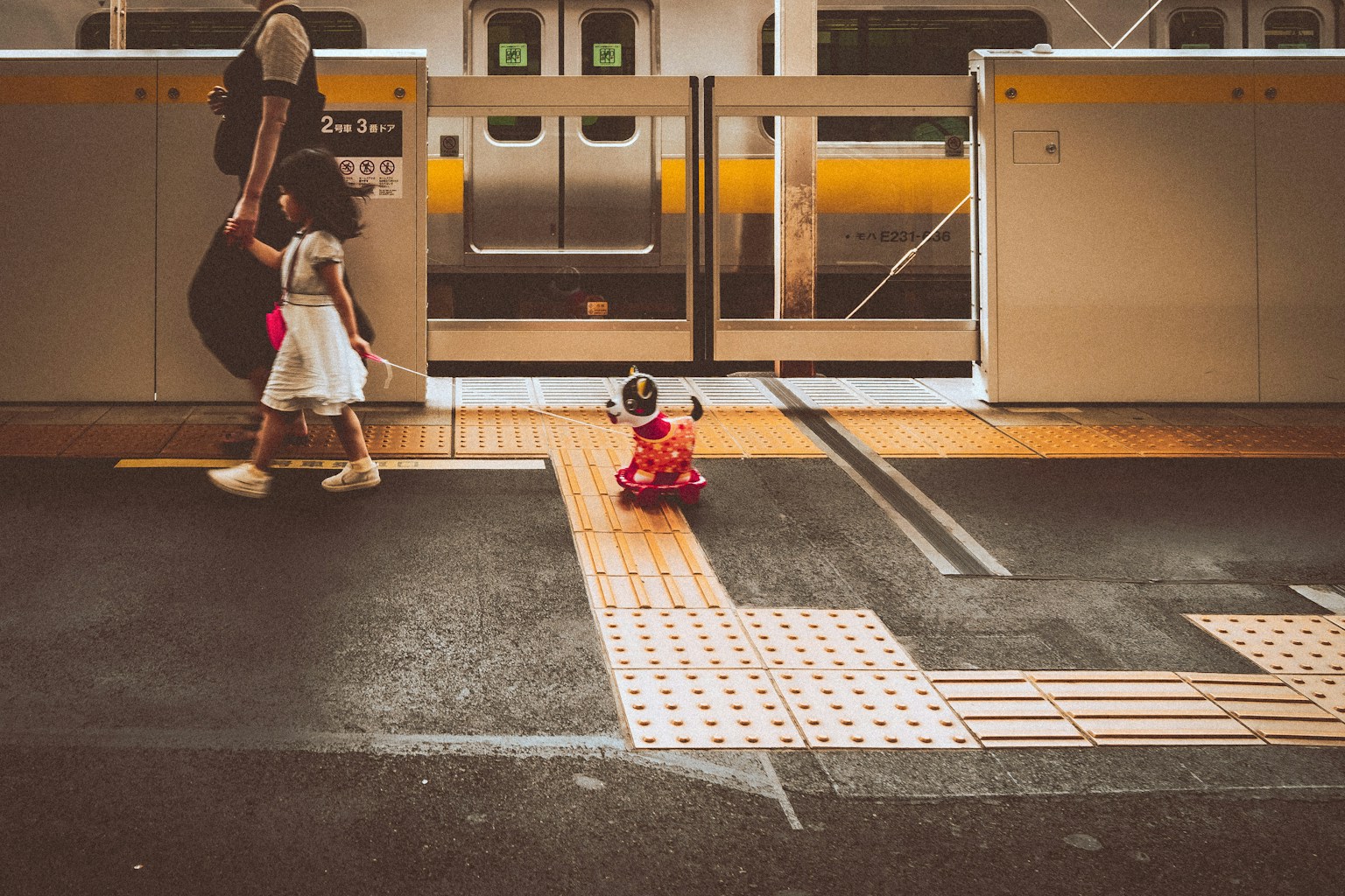 a person and a child walking on a train platform (Photo by Se. Tsuchiya on Unsplash)